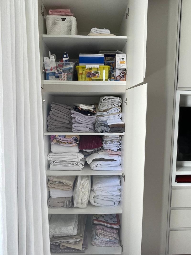 Linen closet with towels and sheets stacked loosely before organizing